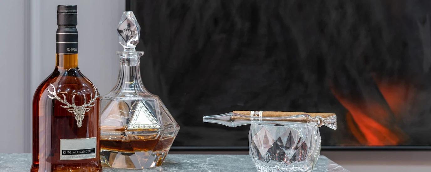 Luxurious display of a whiskey bottle, crystal decanter, and a cigar on a marble table in a sophisticated setting