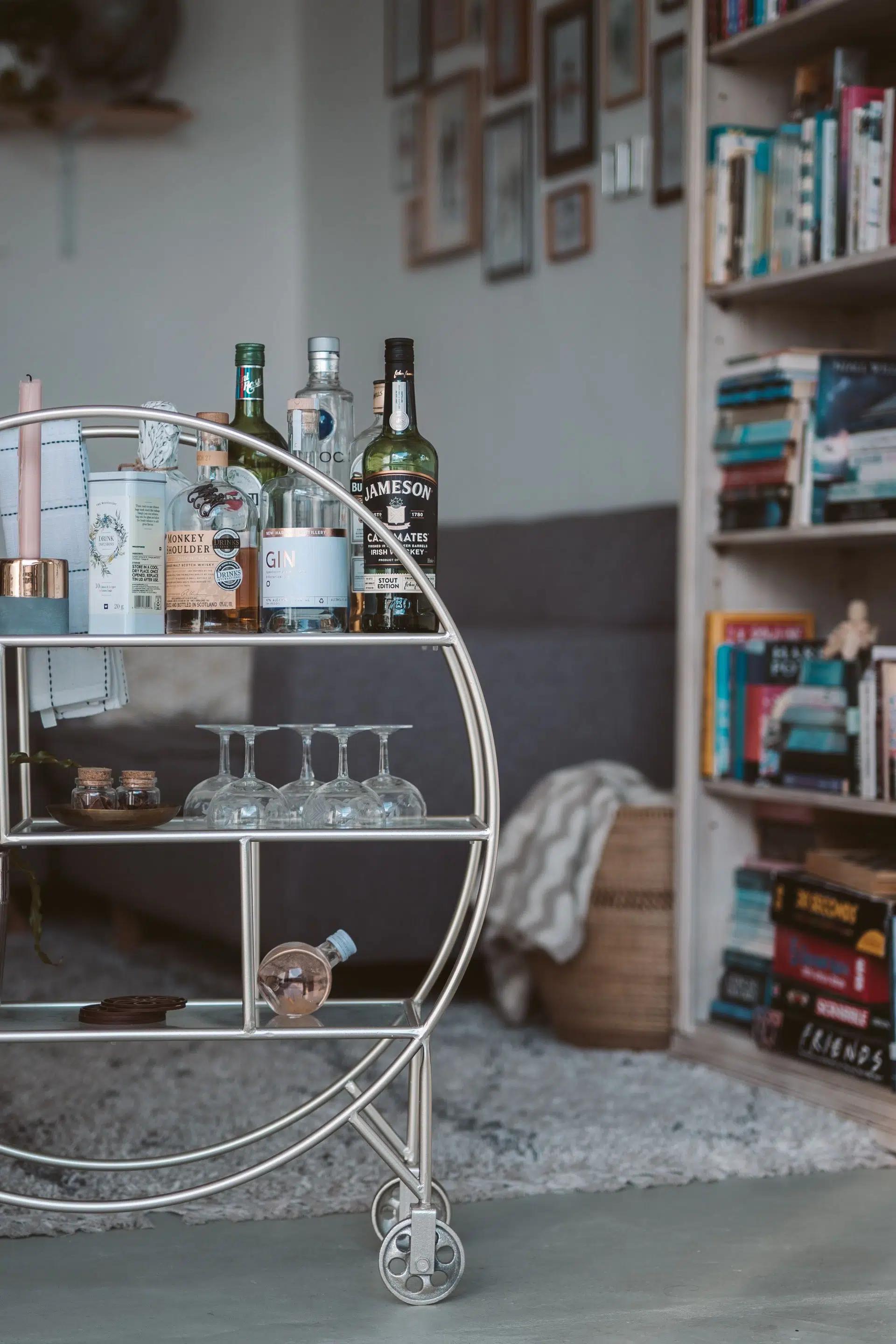 Elegant bar cart with a variety of alcohol bottles, glassware, and stylish home decor in a cozy living room setting