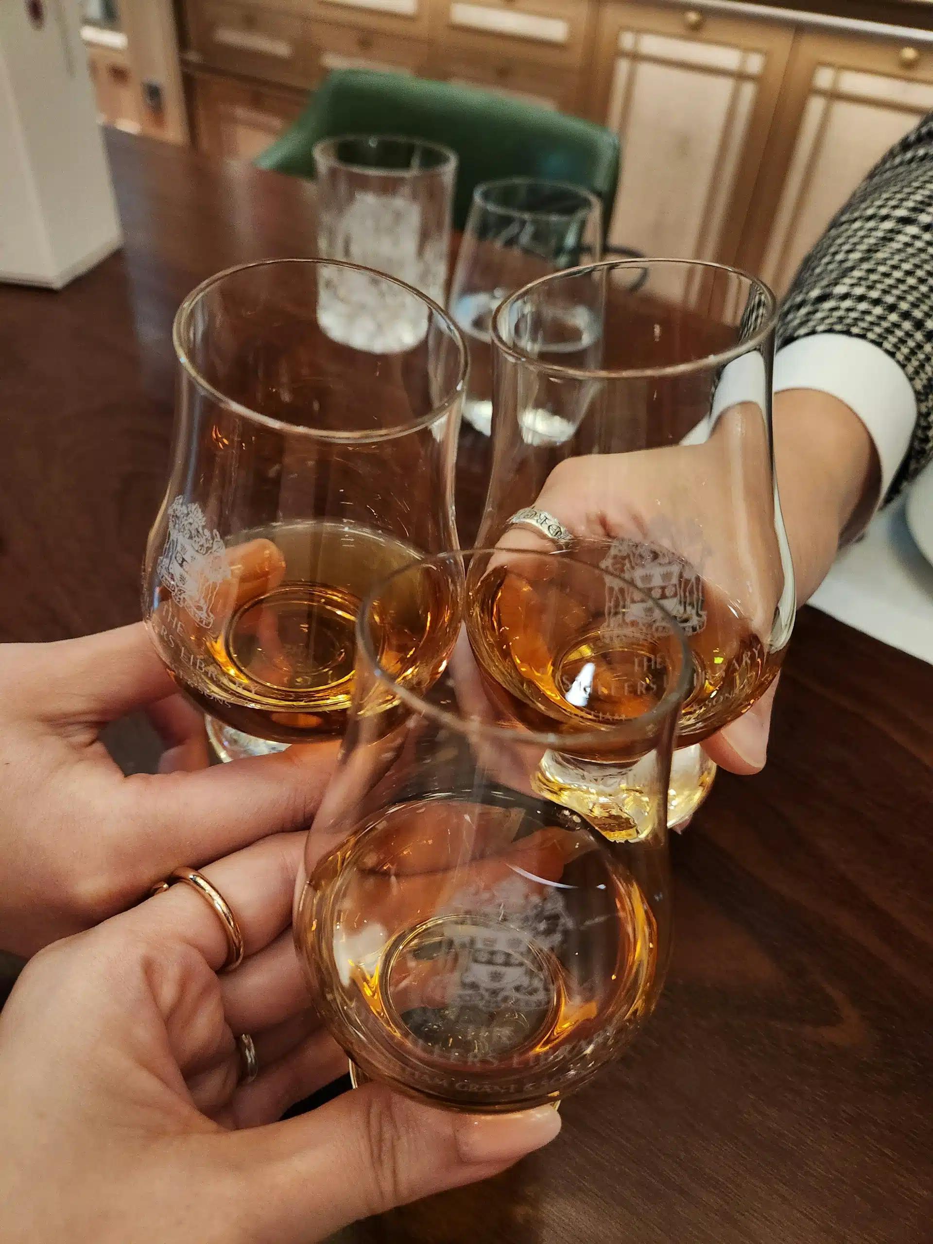 Three hands toasting their whiskey glasses