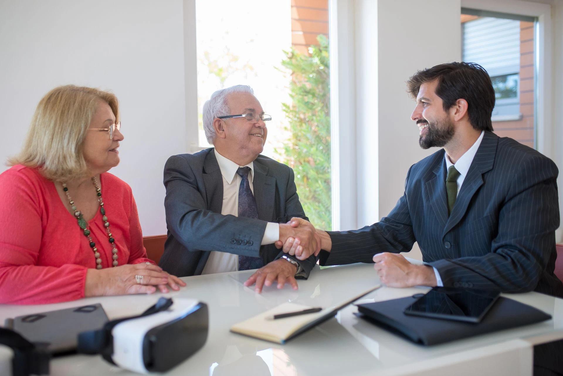 Three business professionals shaking hands during a meeting in an office, symbolizing successful deal-making
