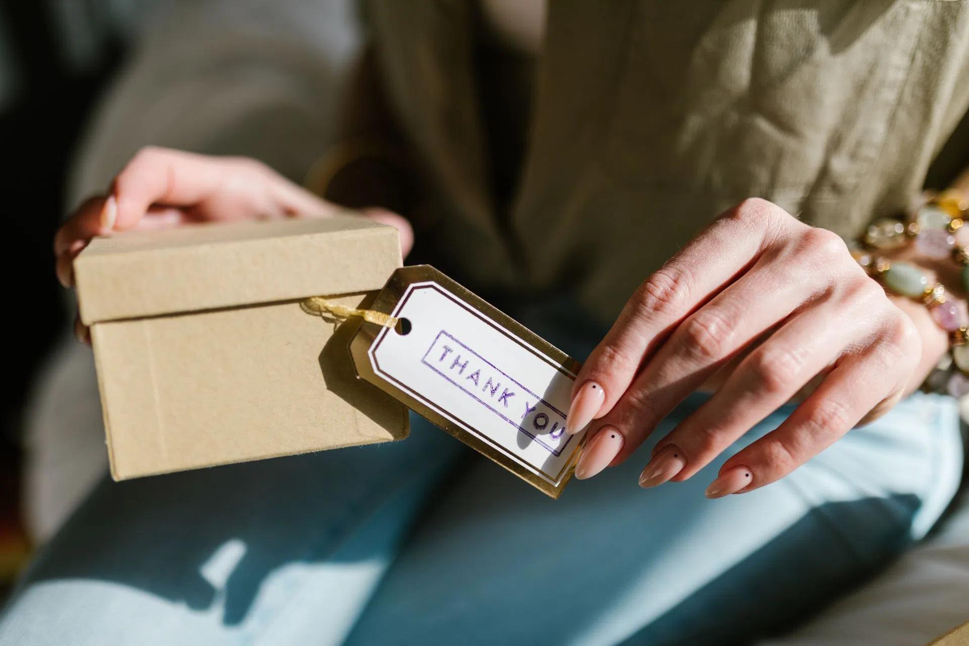 Close-up of hands holding a gift box with a Thank You tag attached, in natural lighting