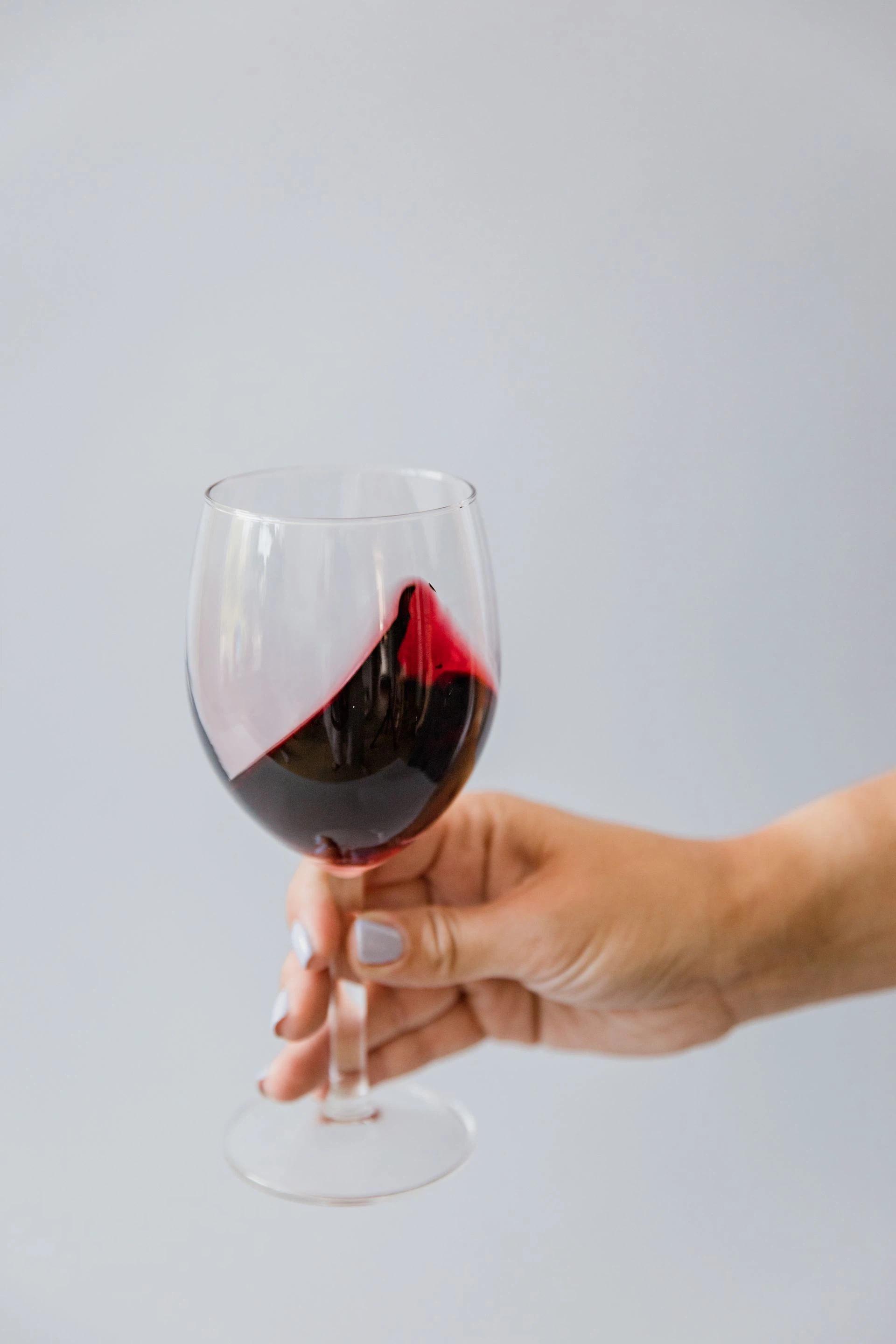 A close-up of a hand swirling a red wine glass against a neutral background.