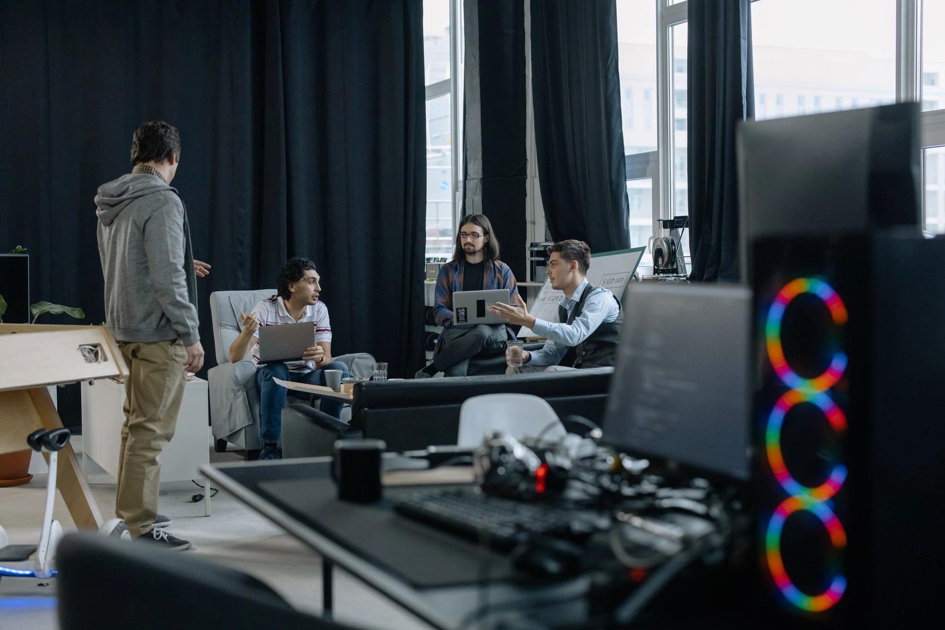 A group of professionals engaged in a casual meeting at a modern office, discussing projects on laptops and tablets