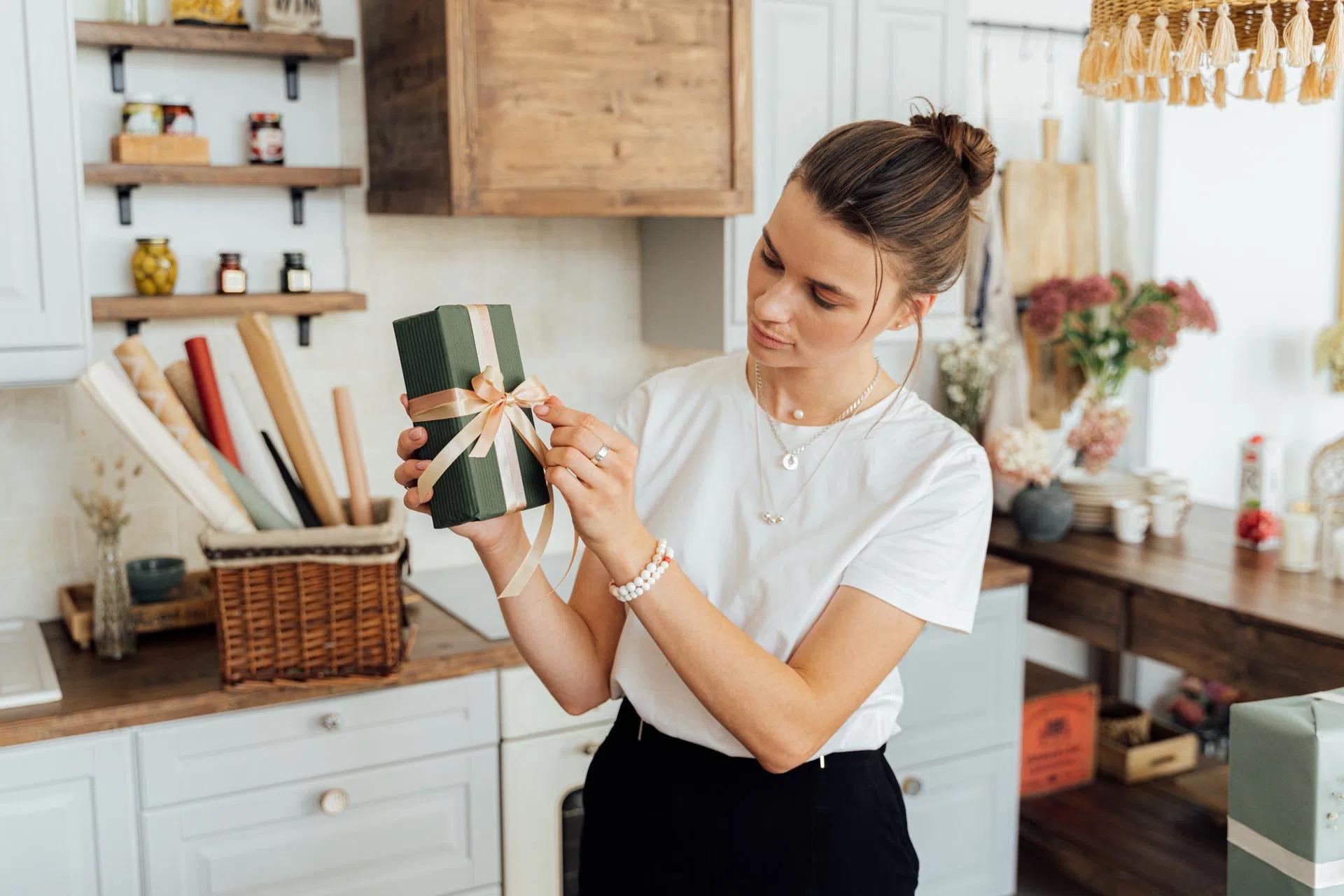 A woman wrapping a gift box with ribbon in a cozy kitchen, capturing a warm and creative atmosphere