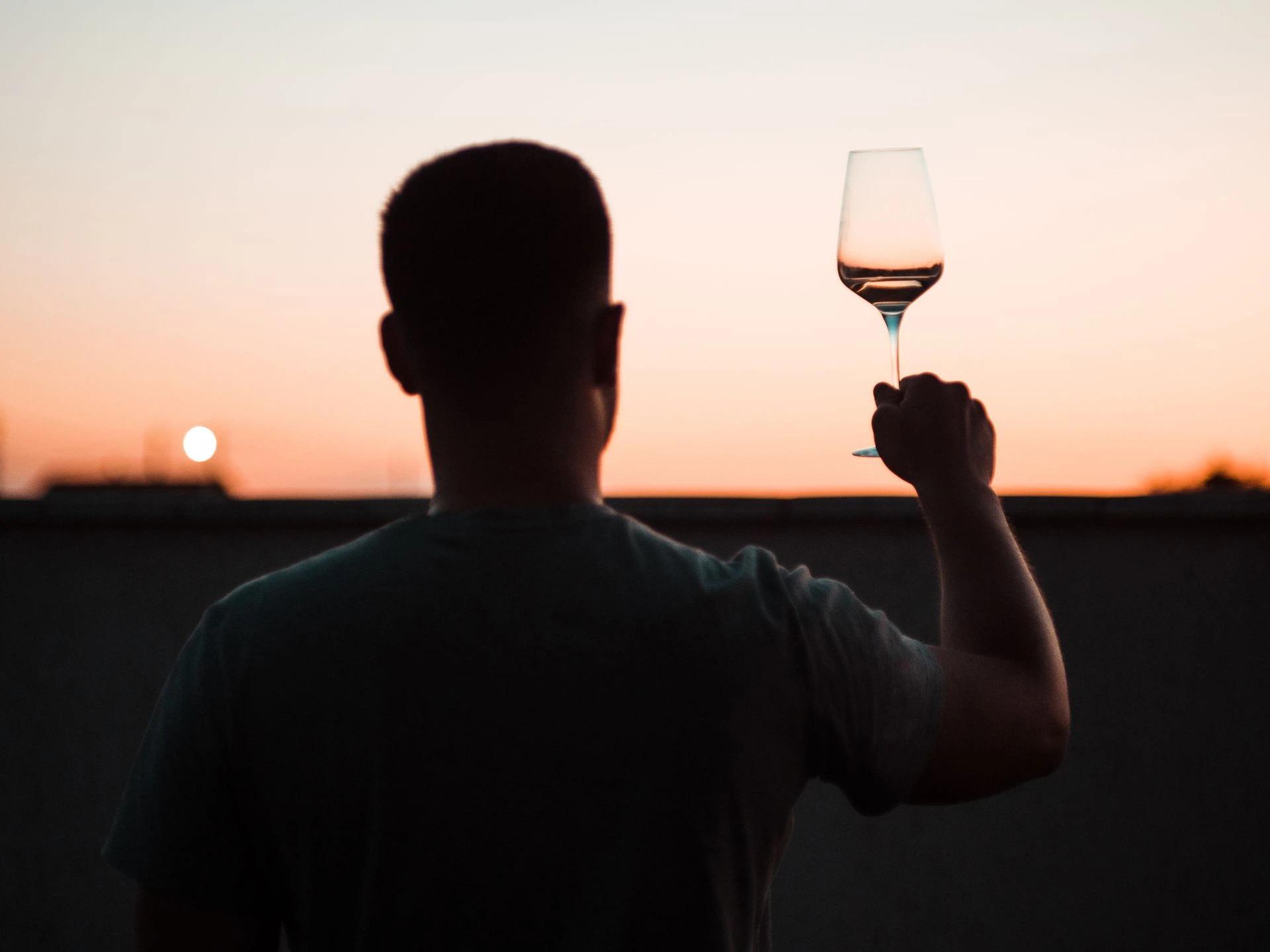 Silhouette of man raising a wine glass at a sunset outdoors.