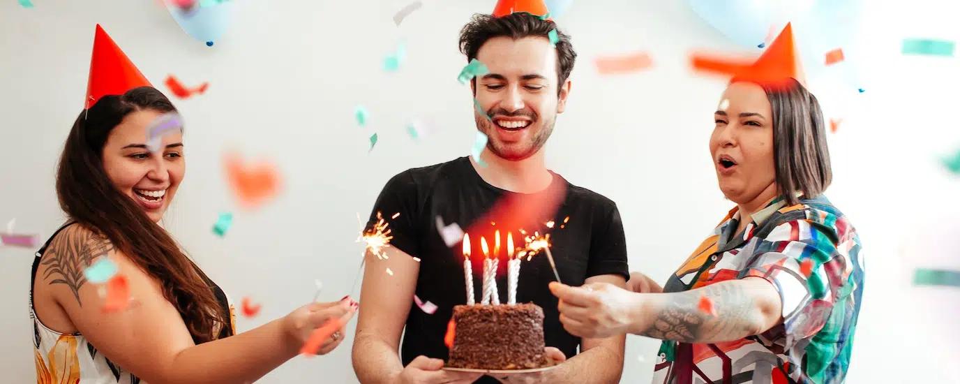 Group of adults celebrating a birthday indoors with cake and confetti, expressing joy and fun