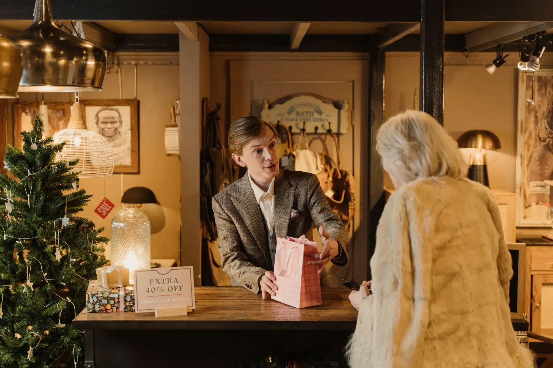 Salesman assisting customer with gift purchase in cozy decorated store during festive sale