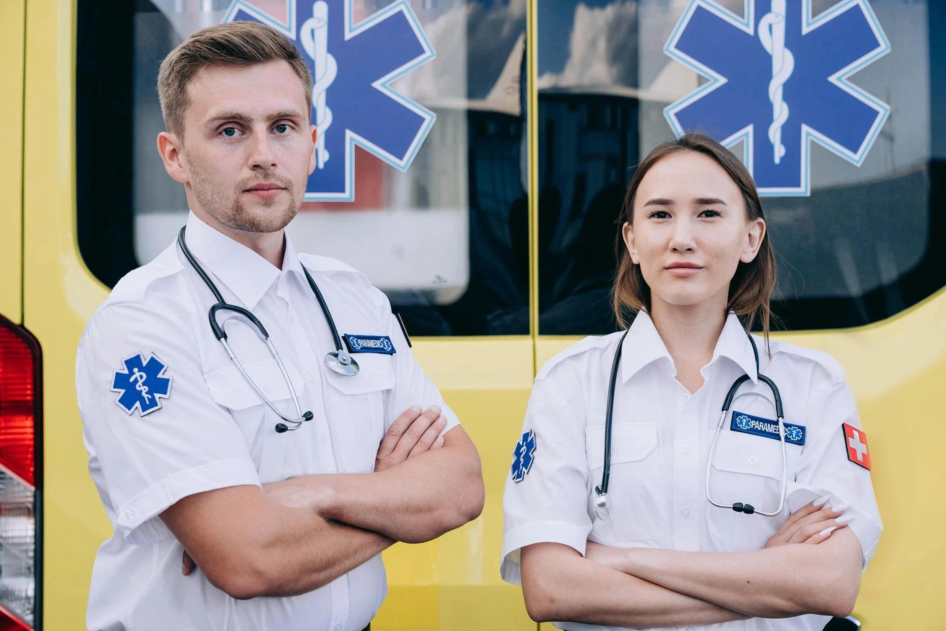 Portrait of two paramedics with stethoscopes standing confidently in front of an ambulance