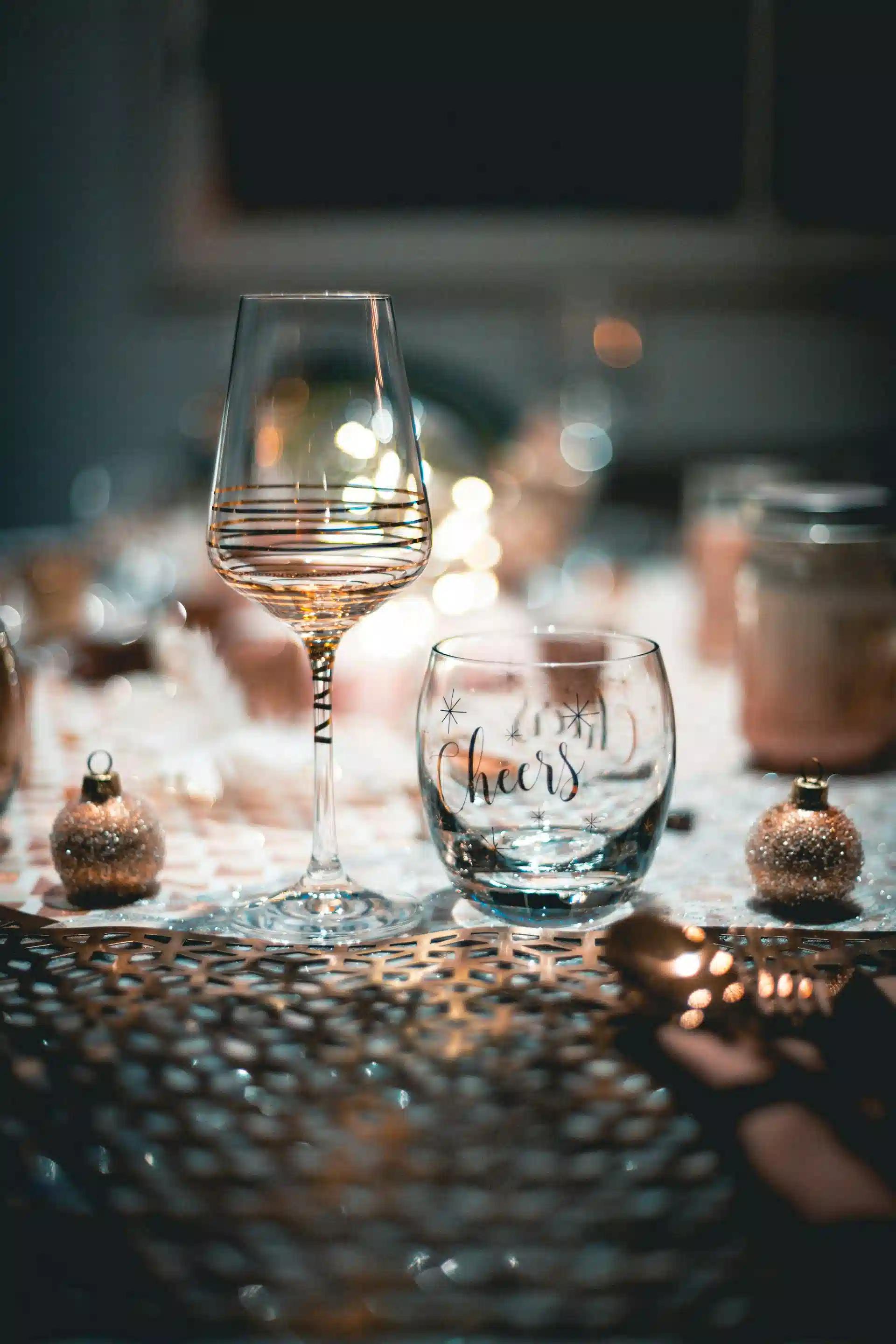 A pair of festively engraved wine glasses surrounded by gliterry ornaments