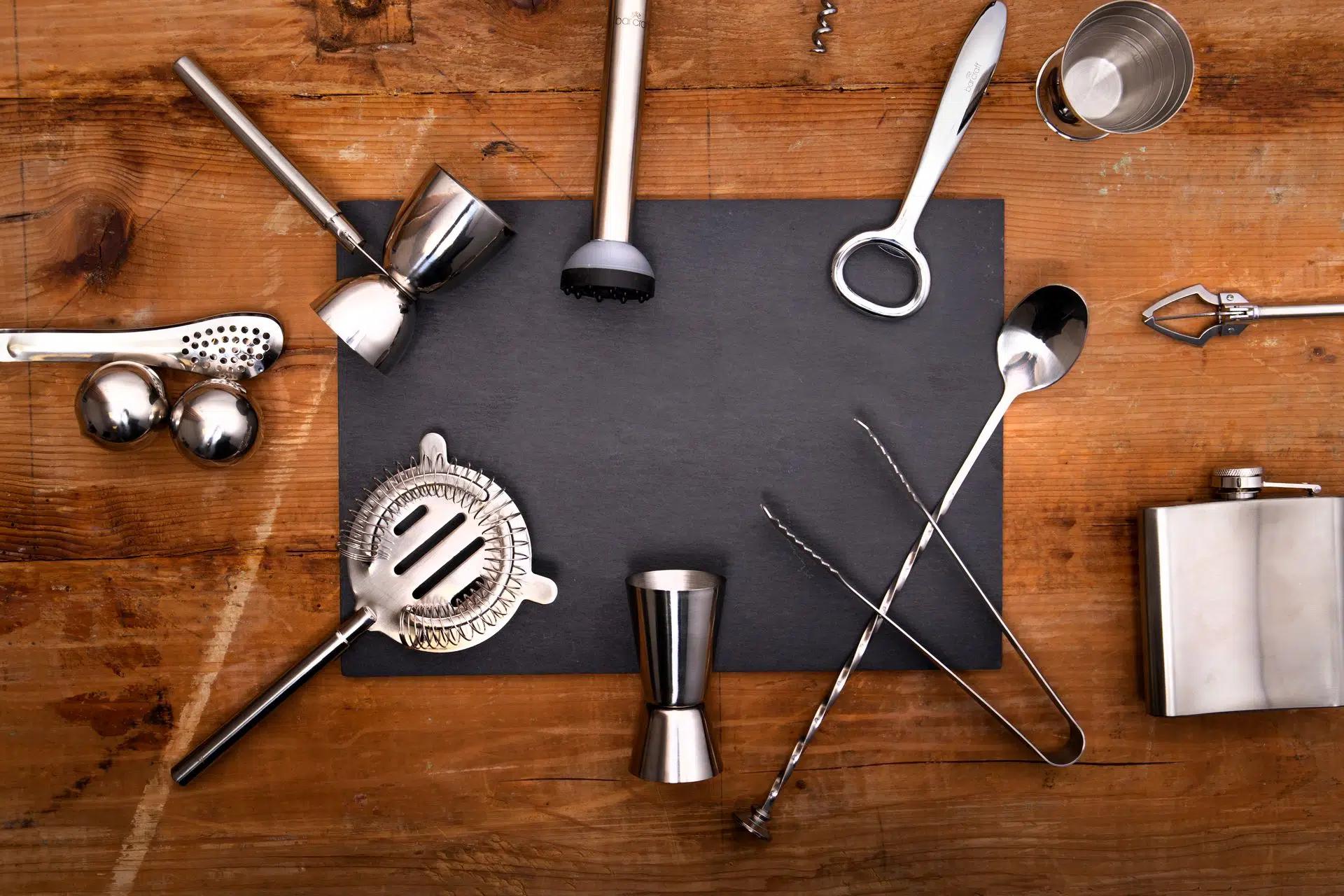 Flatlay of essential stainless steel bar tools arranged on a wooden surface for cocktail making