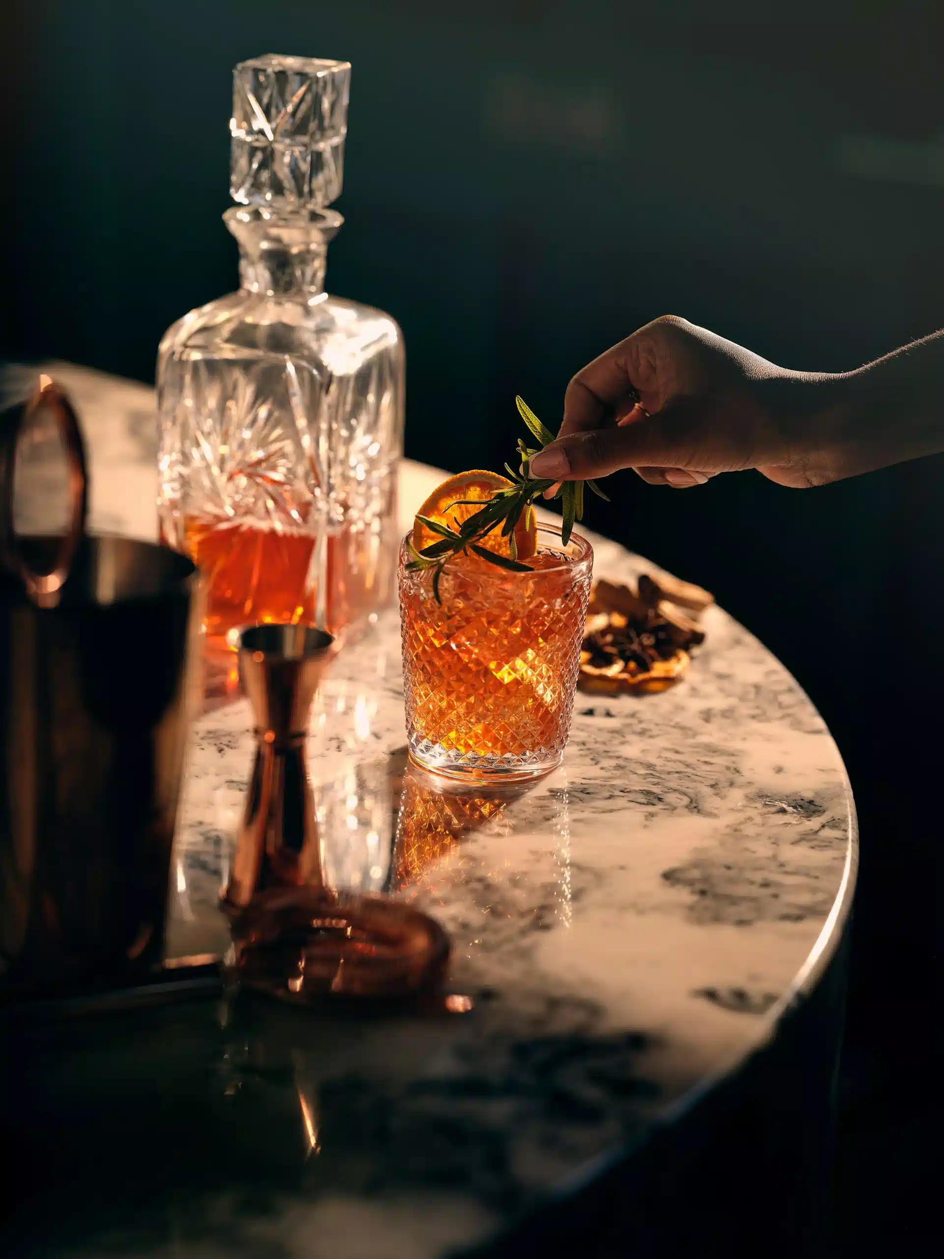 A whiskey decanter and a glass of whiskey cocktail on a marble table
