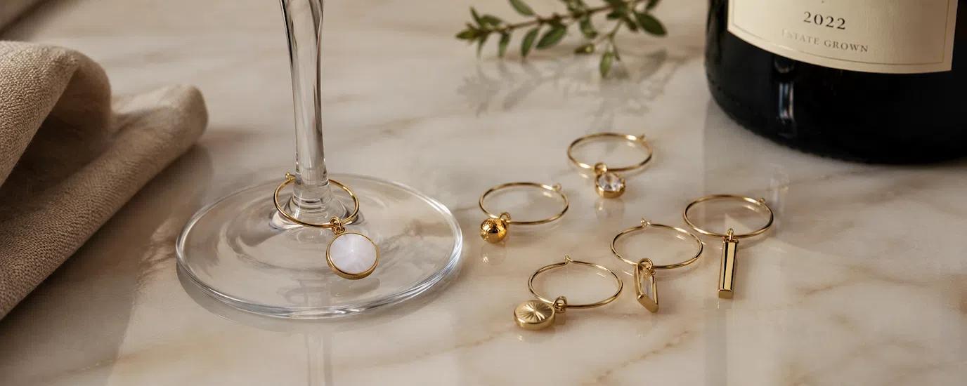 Different wine glass charms in gold finishing at the base of a stemmed wine glass on a table