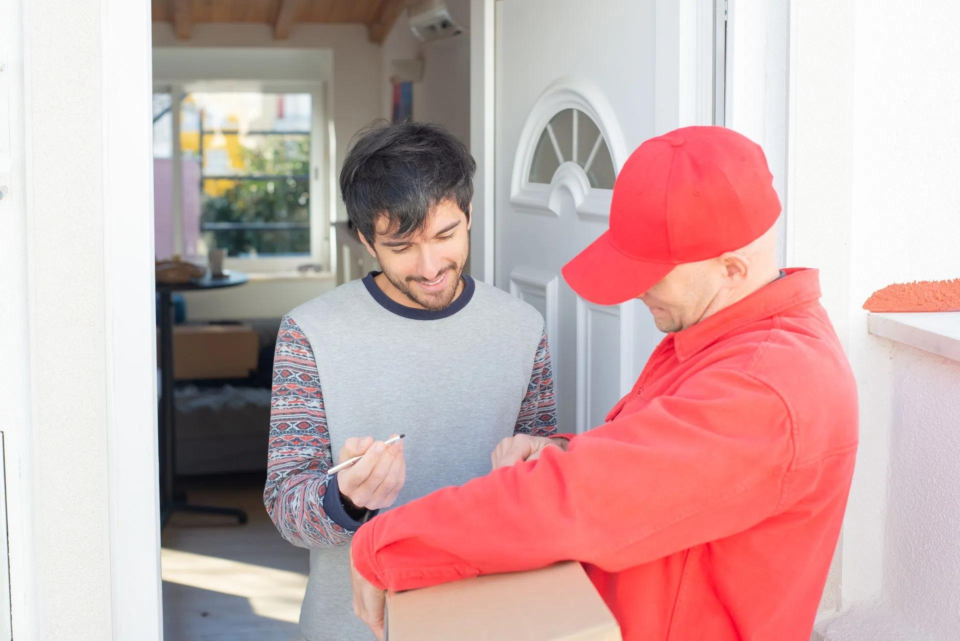 Man signs for a package from a delivery person outside his home, representing a typical doorstep delivery experience