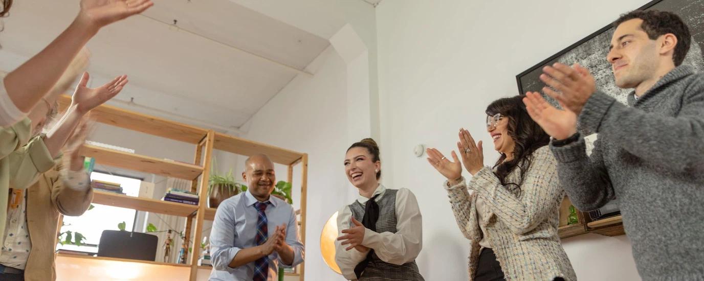 A diverse group of professionals clapping and celebrating in a modern office setting