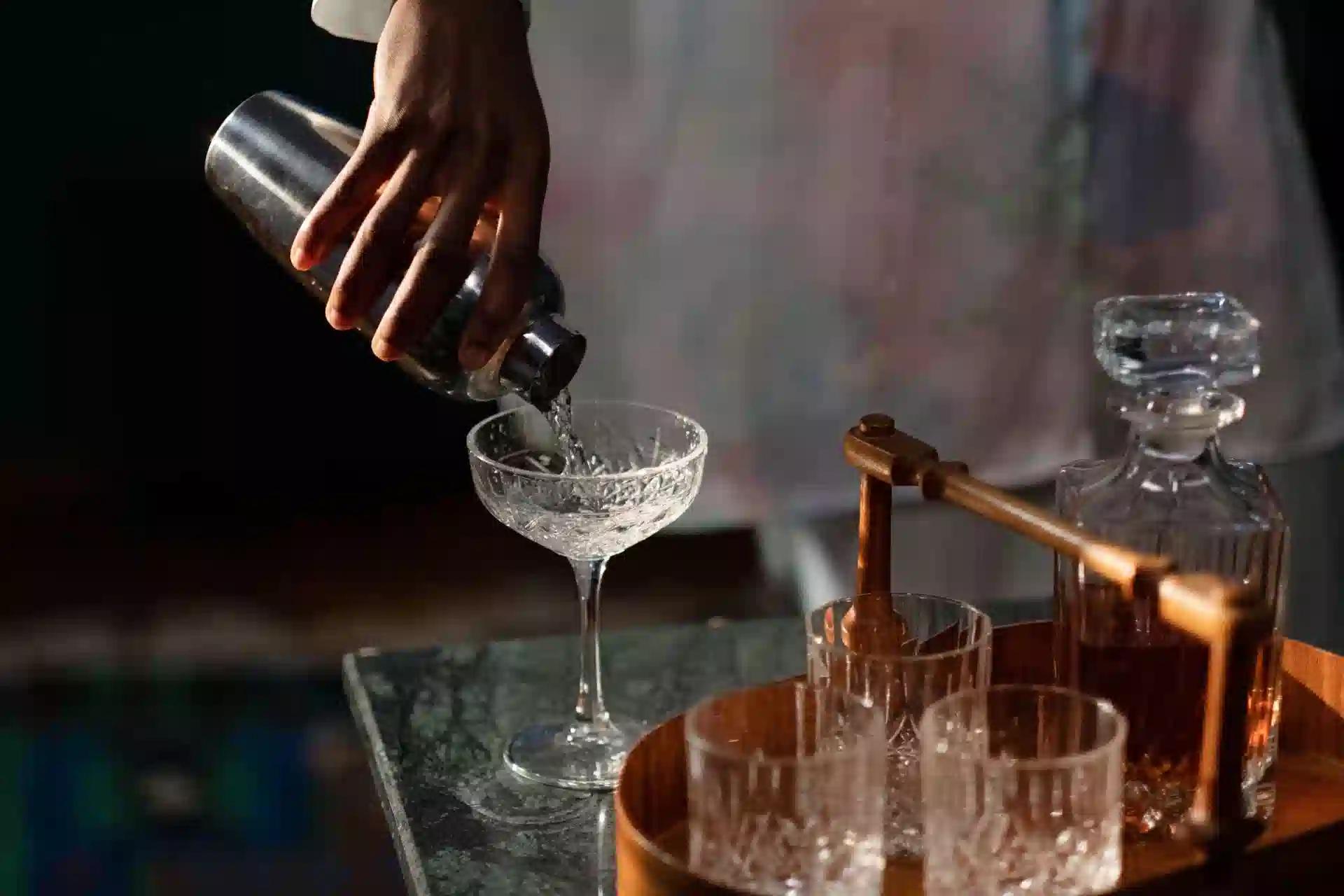 A bartender pours a cocktail into a glass from a shaker, set in a cozy home bar