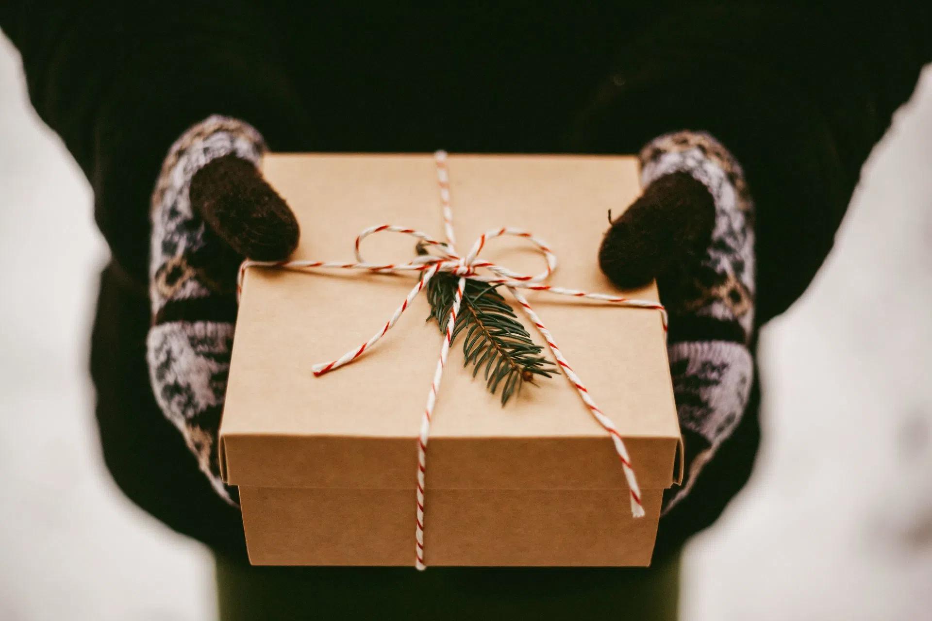 Closeup of hands holding a gift box with a pine sprig, wrapped in festive twine