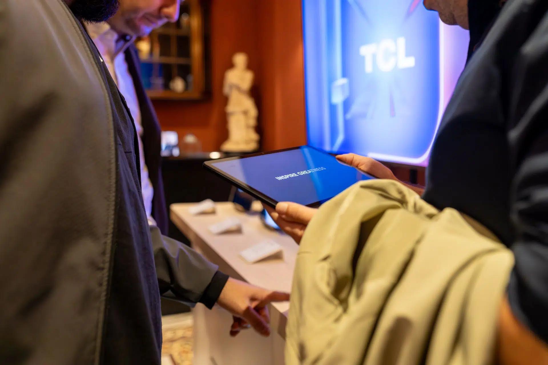 Close-up of individuals exploring a tablet device at a tech exhibit by TCL, highlighting interaction and modern technology