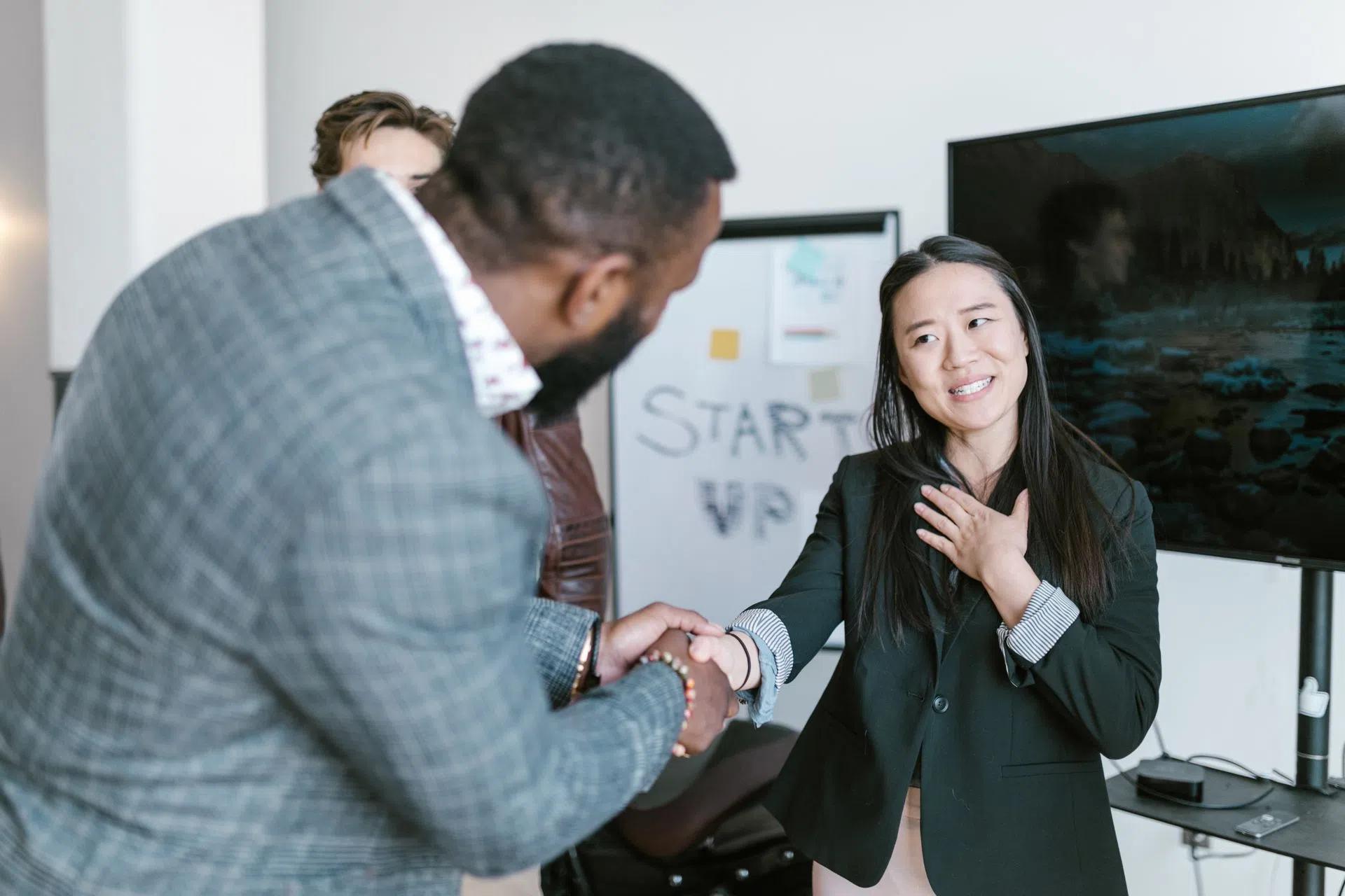 A diverse business team in formal attire exchanging a handshake in a modern office setting, signifying cooperation