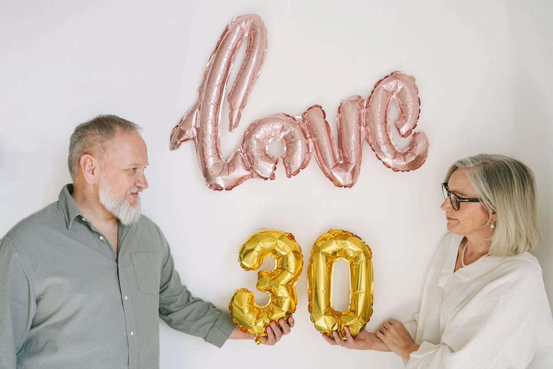 Elderly couple celebrating 30th anniversary with love-themed balloons