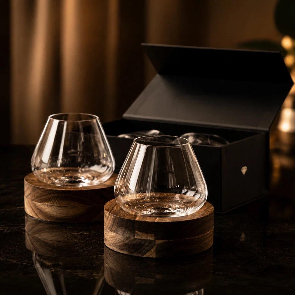 Two empty Aequilibrium glasses on coasters with gift box behind