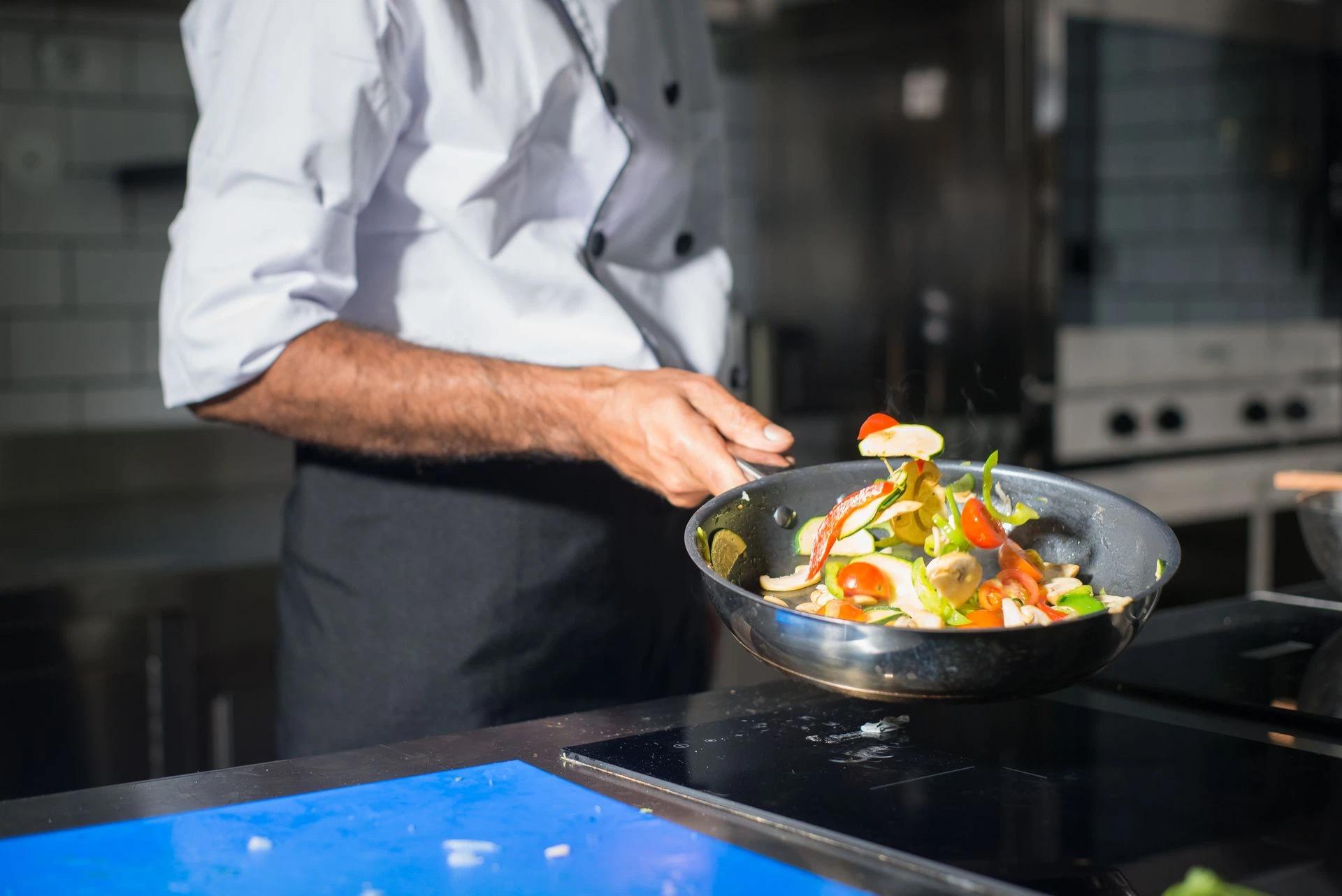 A chef at work in the kitchen sauteeing vegetables in a pan