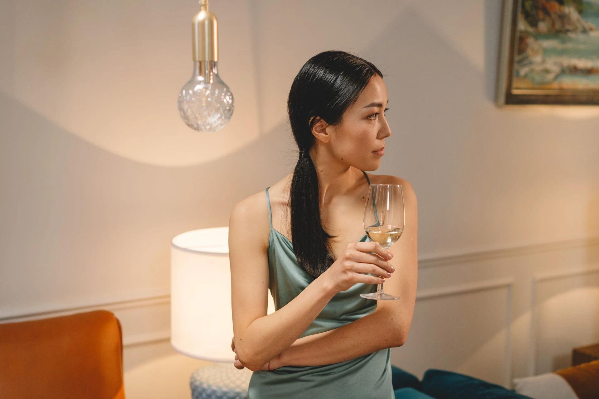Sophisticated woman in elegant dress holding a glass of wine indoors under warm lighting