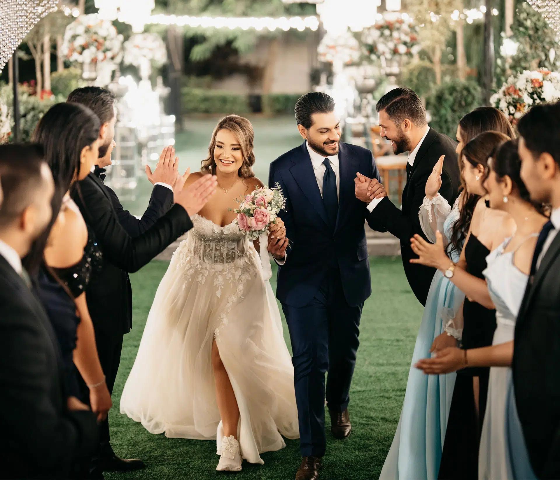 Bride and groom joyfully walking through cheering guests at a vibrant outdoor wedding reception
