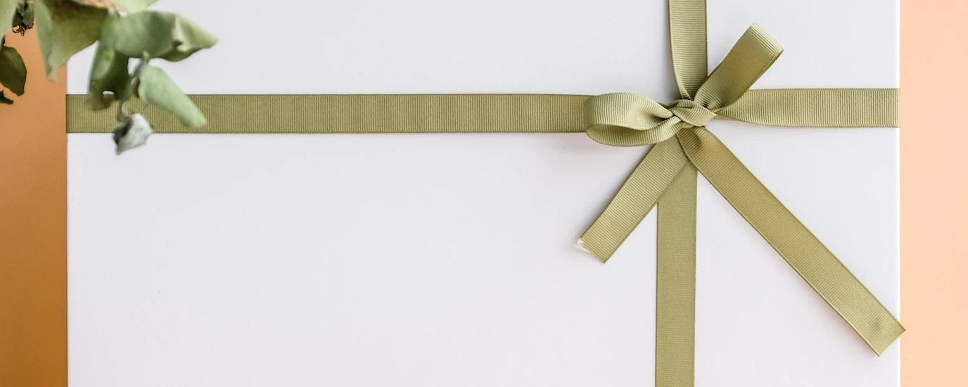 A white gift box with a gold ribbon against a peach background