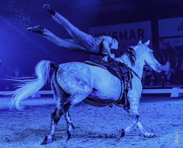 Trickrider in volle sprong over een galopperend paard