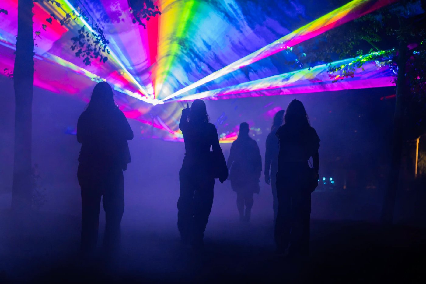 Bezoekers wandelen in silhouet onder een dak van lasers