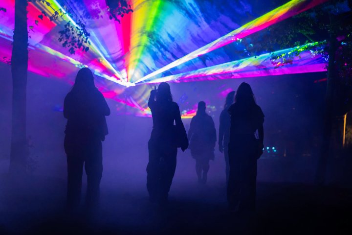 Bezoekers wandelen in silhouet onder een dak van lasers
