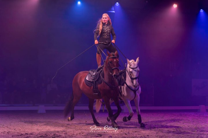 Artieste staat rechtop op twee paarden