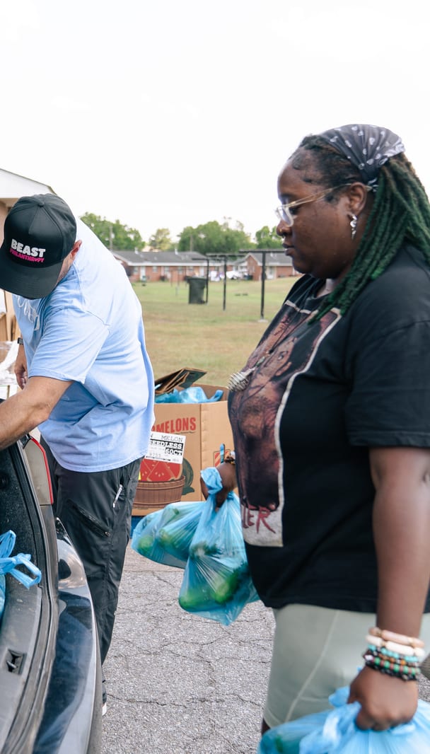 Volunteers loading bags of groceries into an open car trunk
