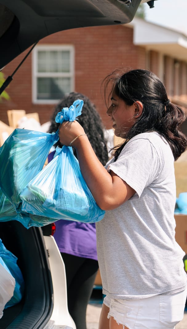 A volunteer lifting bags into an open trunk