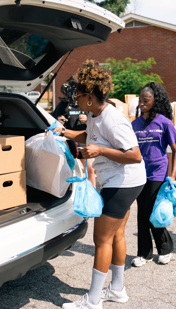 A volunteer with bags of groceries beside a car
