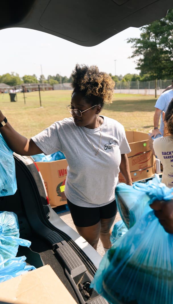 A volunteer passing bags from the back of a car