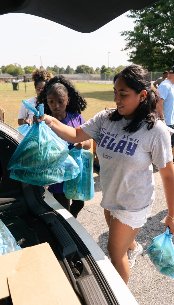 A volunteer carrying bags of groceries to a waiting car