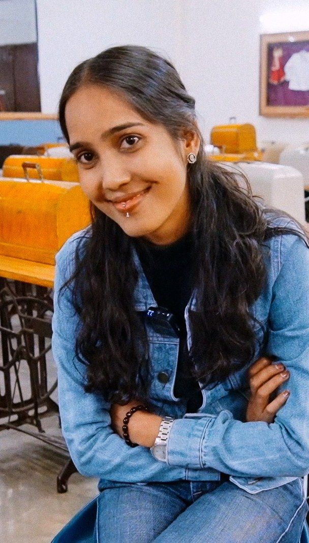Sheetal sitting in a tailoring workshop lined with sewing machines