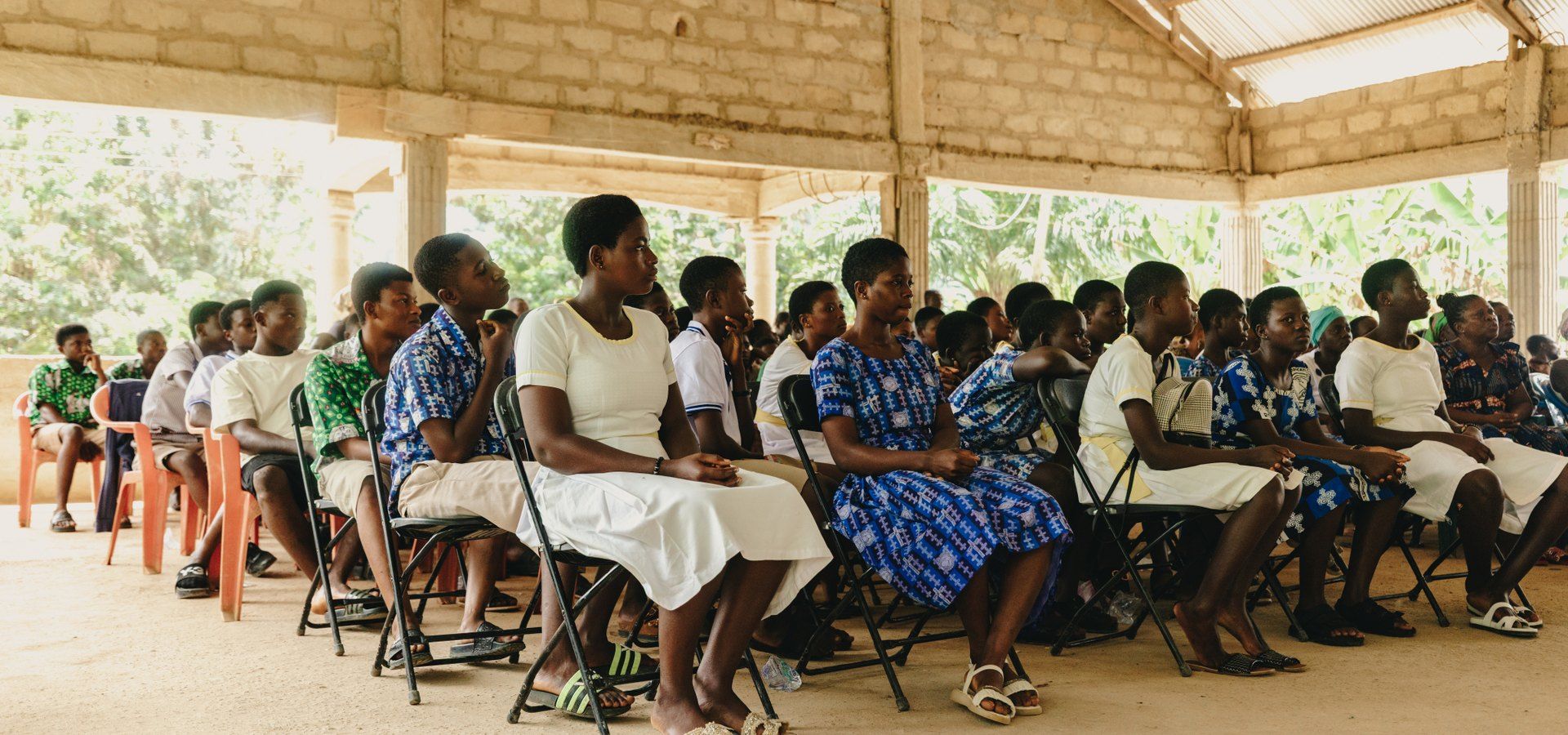 Students and community members seated together at a gathering in a Ghanaian village