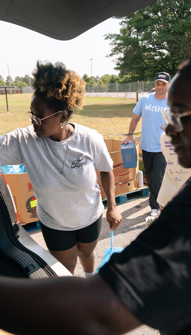 A volunteer reaching for bags in a loaded trunk