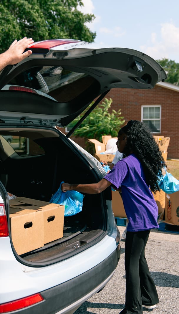 A volunteer reaching into a car trunk packed with groceries