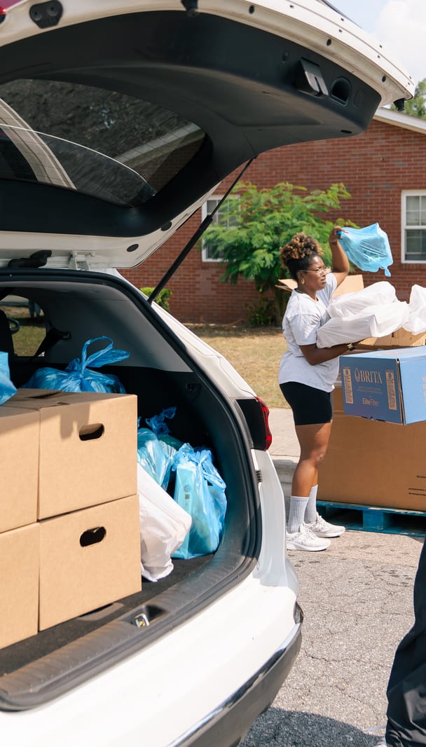 A volunteer carrying a box past the line of cars