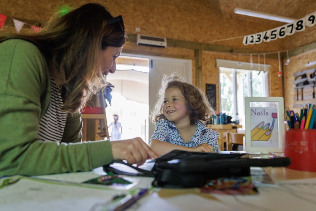 Teacher interacting with a young girl in a classroom at Mill Hill Pre-Prep, both smiling as they engage in a creative indoor activity, fostering a joyful learning environment.