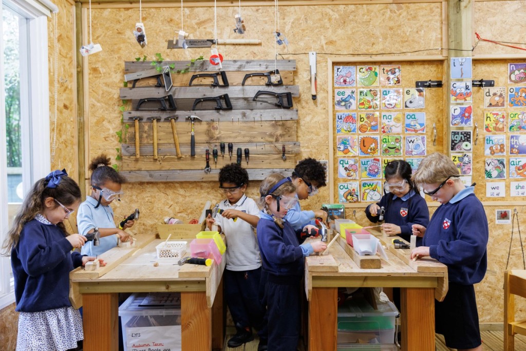 Children at Mill Hill Pre-Prep engaged in a woodworking activity, wearing safety goggles and using tools in a hands-on learning environment.