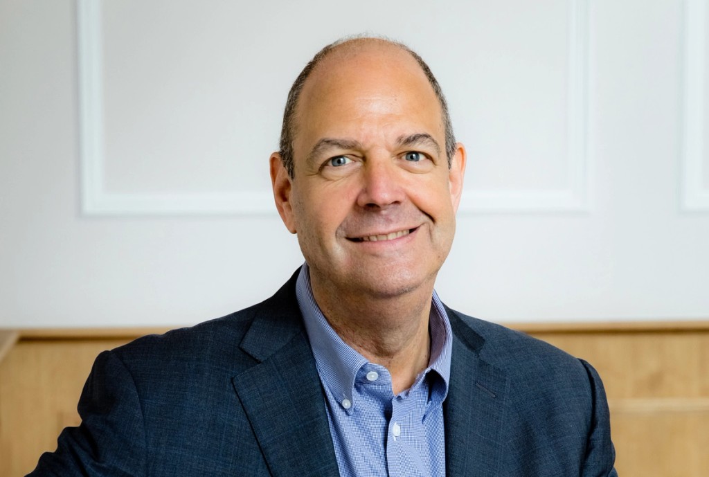 Portrait of the Chair of Governors at Mill Hill School, smiling in a formal setting, wearing a dark suit and light blue shirt.