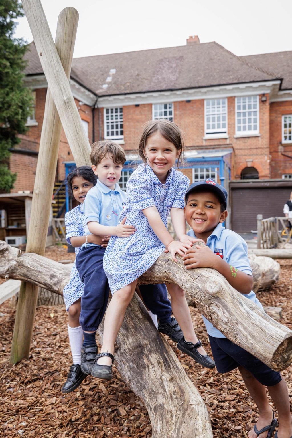 Children in school uniforms play on a wooden structure in Grimsdell, Mill Hill Pre-prep School's playground, enjoying outdoor activities and smiling together.