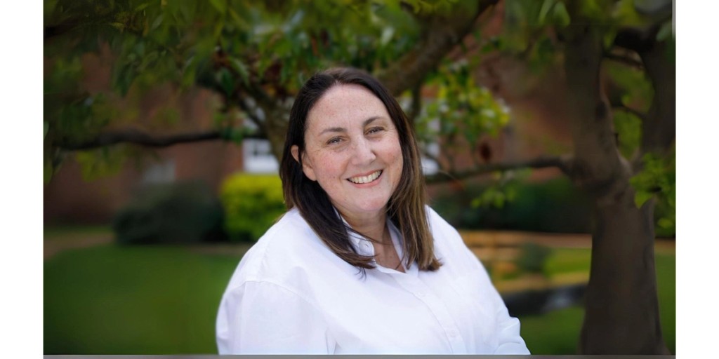 Portrait of the Senior Deputy Head at Mill Hill School, smiling outdoors in a professional headshot, wearing a white shirt with a natural green background.