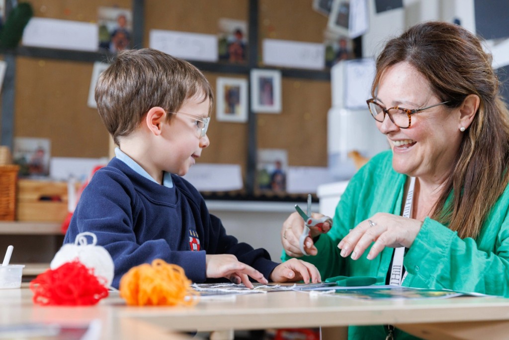 A teacher and a young child at Mill Hill Pre-Prep engage in a fun crafting activity, smiling as they work together on a creative project in the classroom.