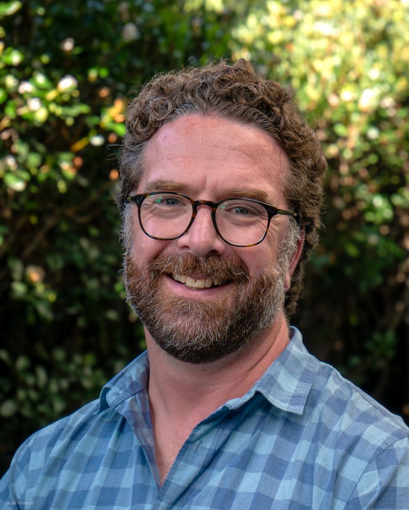 Josh smiling with glasses and a blue checked shirt