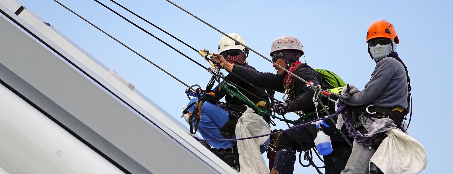 Rope-access workers in harnesses and hard hats climbing a steel structure